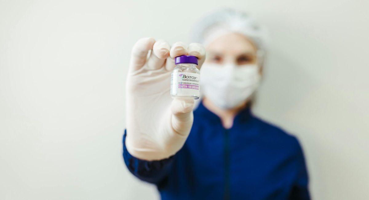 Healthcare worker holding a Botox vial in a clinical setting, wearing protective gear.